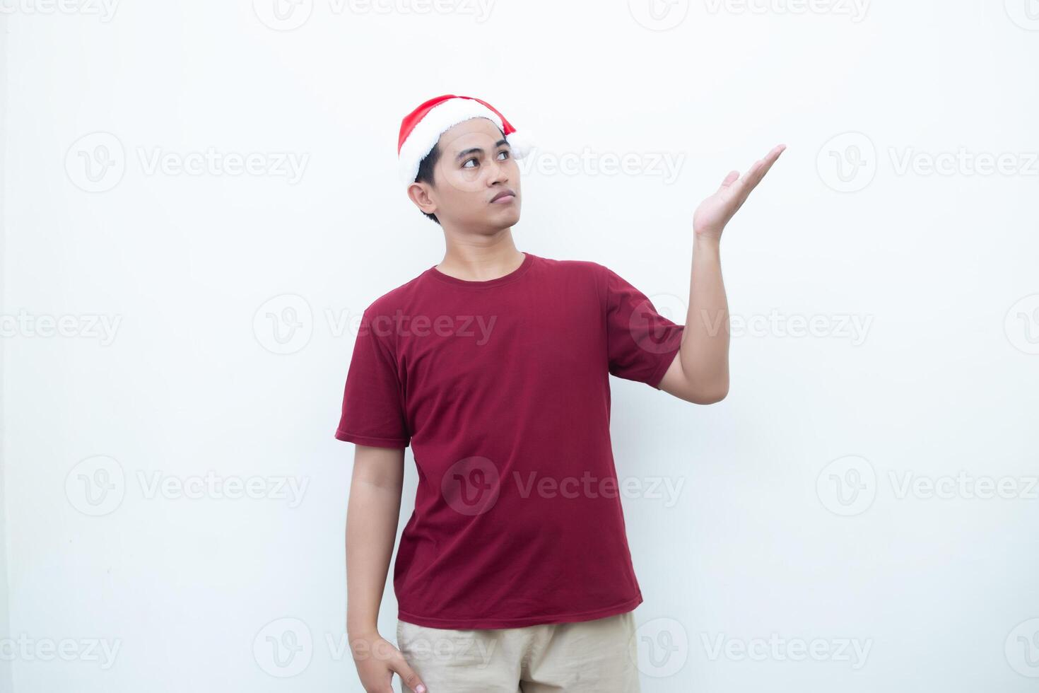 Young Asian man wearing a Santa Claus hat smiling, shock and pointing to her side isolated by white background for visual communication photo