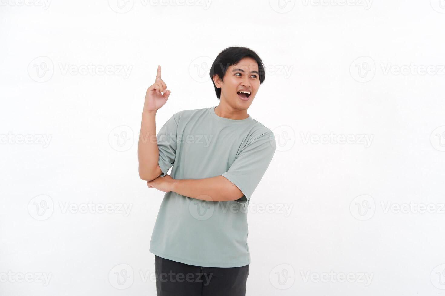 Excited Asian male employee wearing a tshirt pointing at the copy space above him, isolated by white background photo