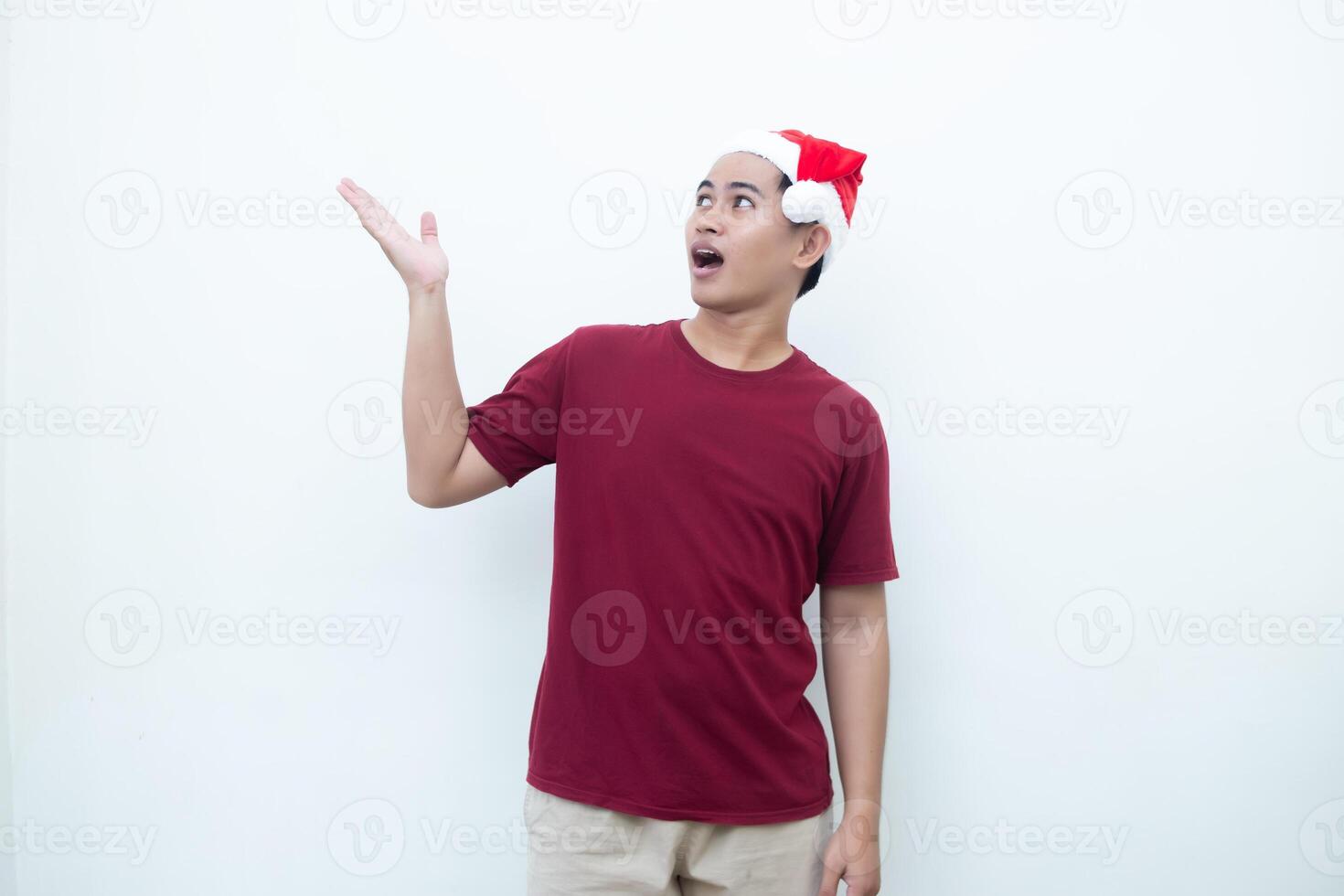 Young Asian man wearing a Santa Claus hat smiling, shock and pointing to her side isolated by white background for visual communication photo