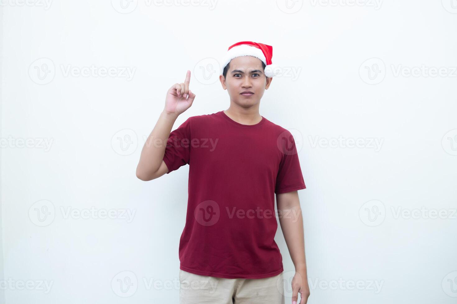 joven asiático hombre vistiendo un Papa Noel claus sombrero sonriente, conmoción y señalando a su lado aislado por blanco antecedentes para visual comunicación foto