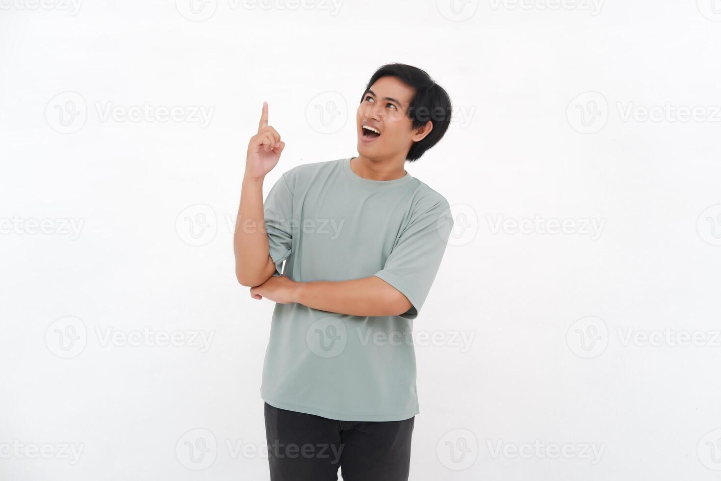 Excited Asian male employee wearing a tshirt pointing at the copy space above him, isolated by white background photo
