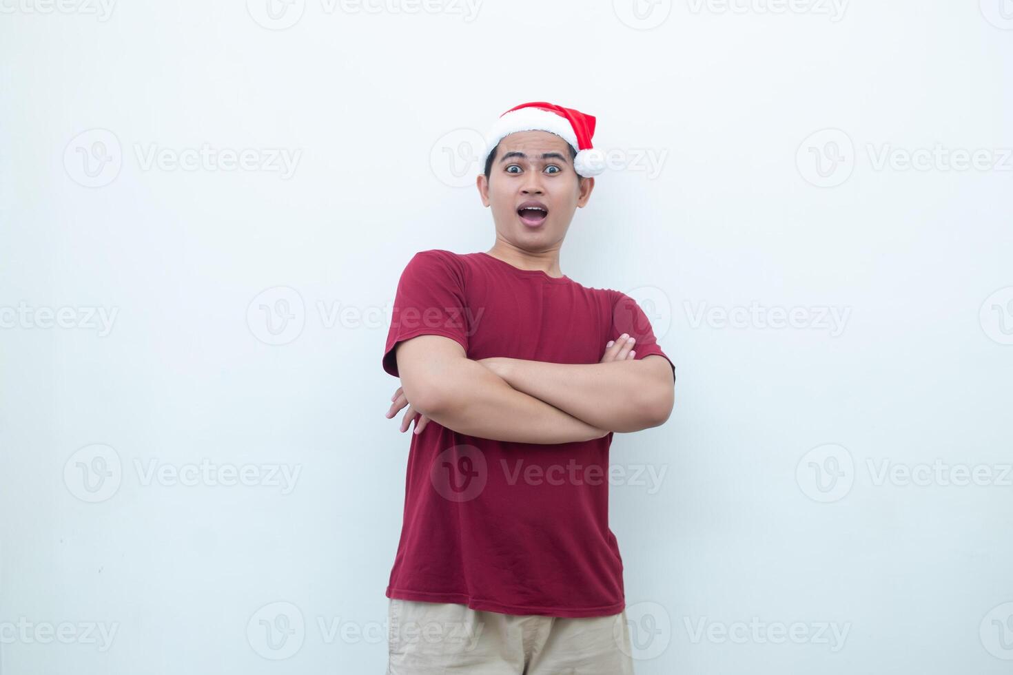 Young Asian man wearing a Santa Claus hat crossing his arms while smiling, shock and laughing with a white background for visual communication photo