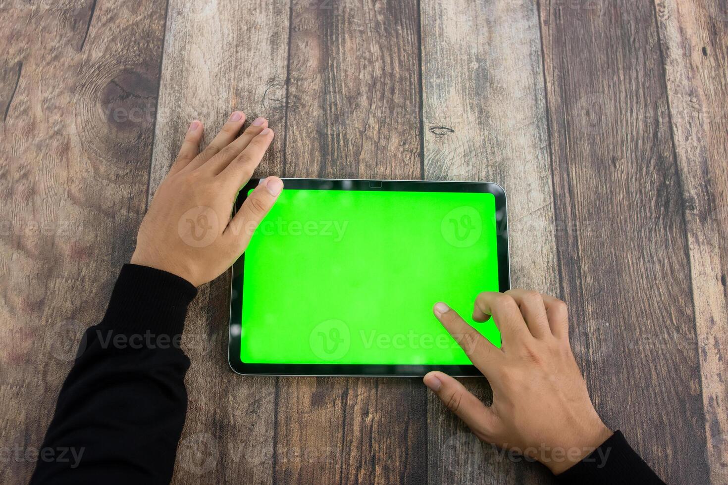 Mock up of a hand holding an iPad tablet with a greenscreen against a wooden texture background photo
