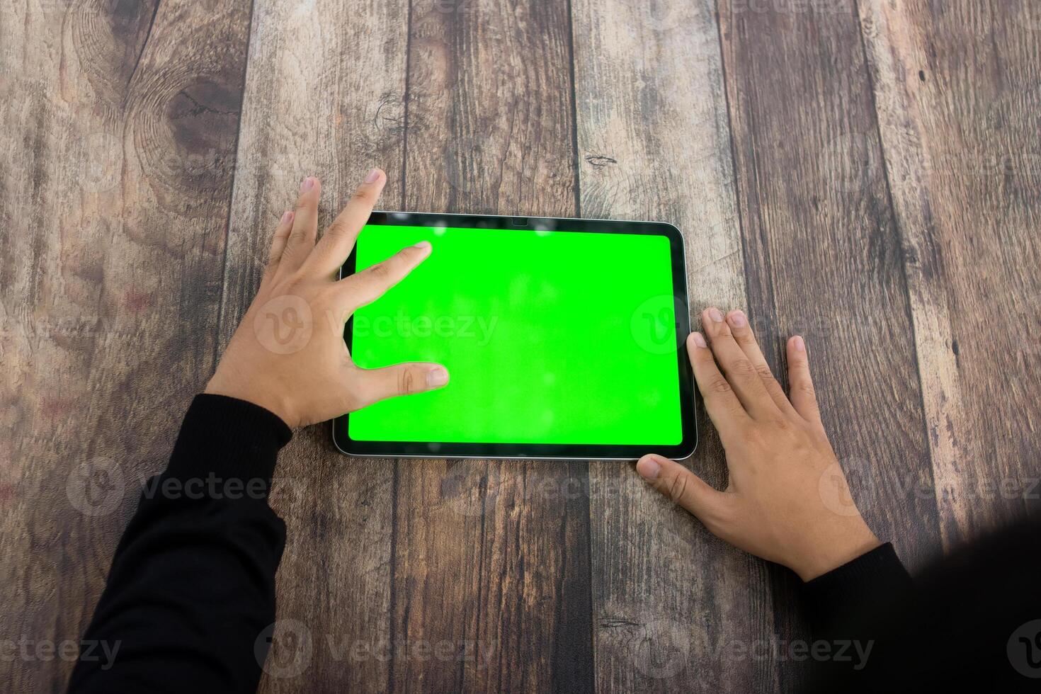 Mock up of a hand holding an iPad tablet with a greenscreen against a wooden texture background photo