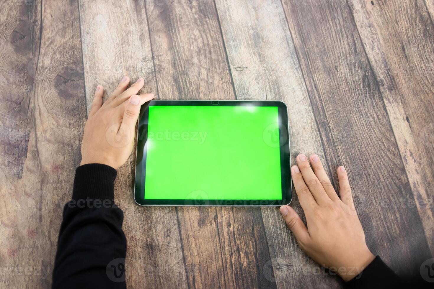 Mock up of a hand holding an iPad tablet with a greenscreen against a wooden texture background photo