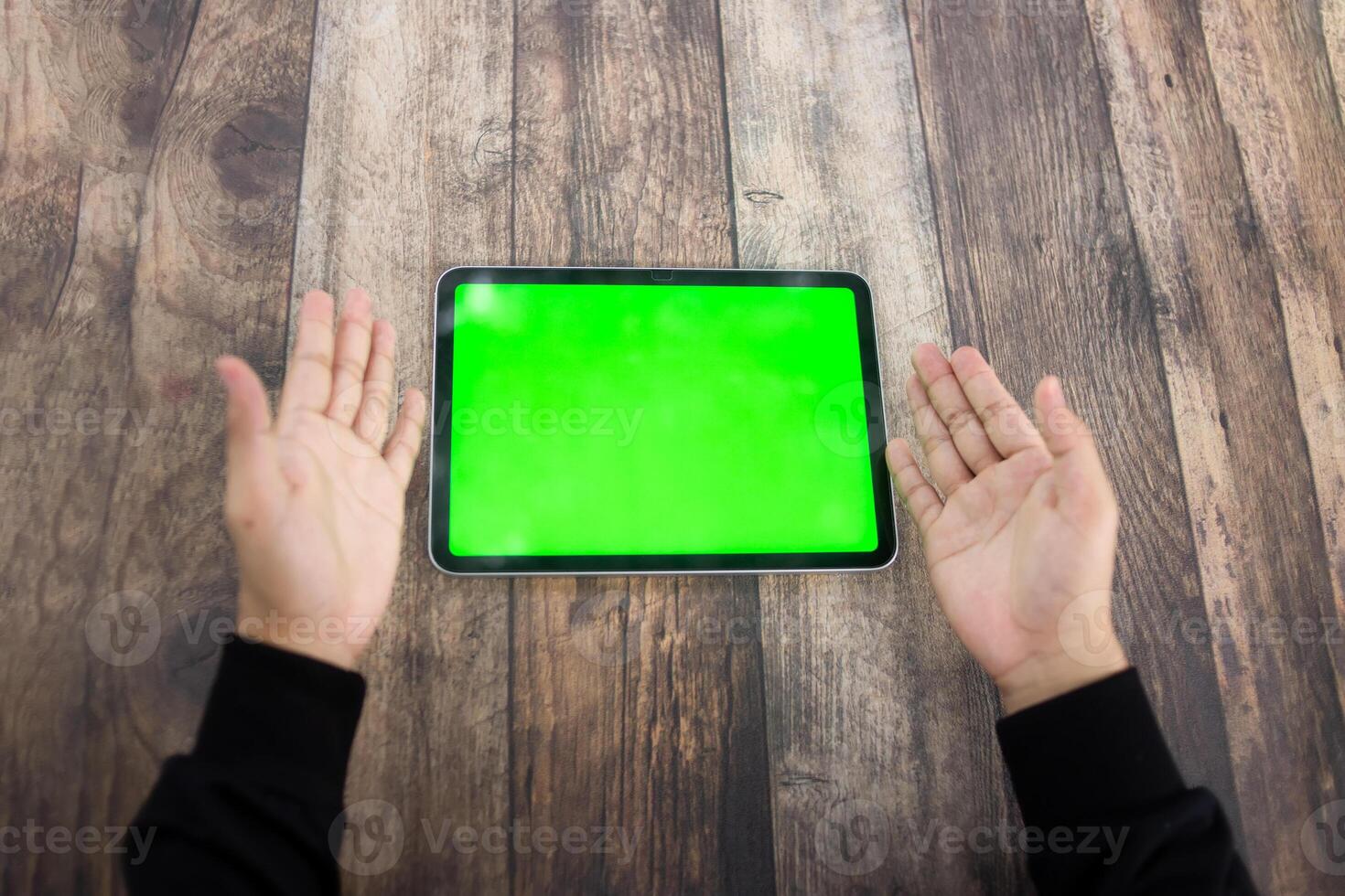 Mock up of a hand holding an iPad tablet with a greenscreen against a wooden texture background photo