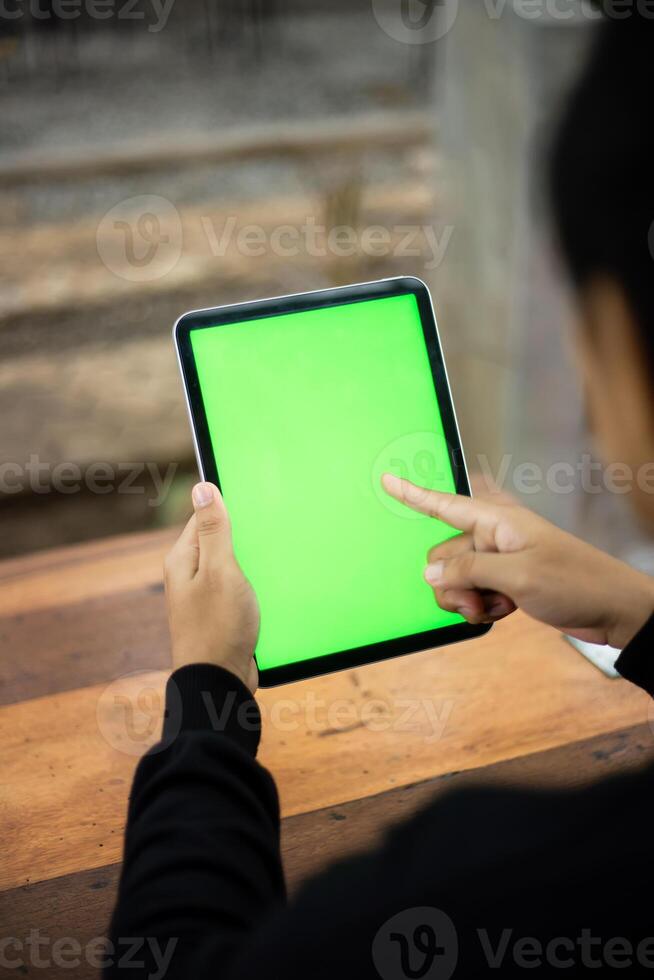 Mock up photo of a close up shot featuring a mans hand holding an iPad tablet with a green screen against the background of a wood cafe table