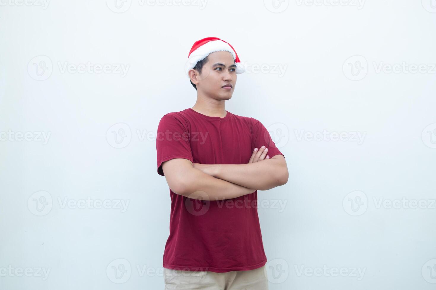 Young Asian man wearing a Santa Claus hat crossing his arms while smiling, shock and laughing with a white background for visual communication photo