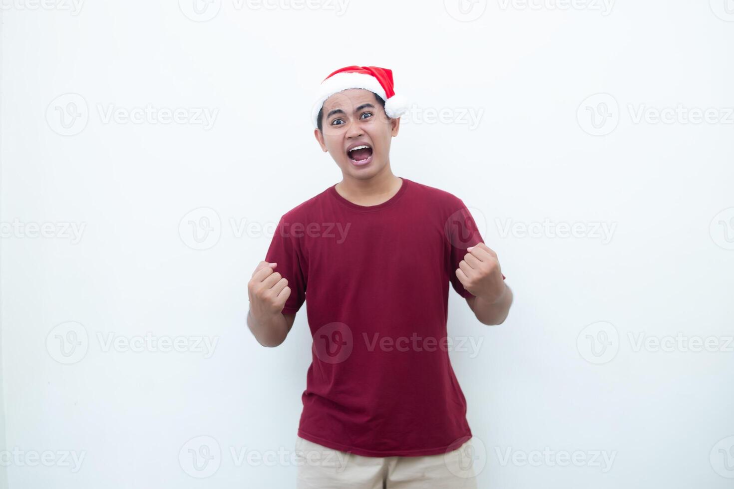 joven asiático hombre vistiendo un Papa Noel claus sombrero agarre ambos manos con entusiasmo y ira aislado por un blanco antecedentes para visual comunicación foto