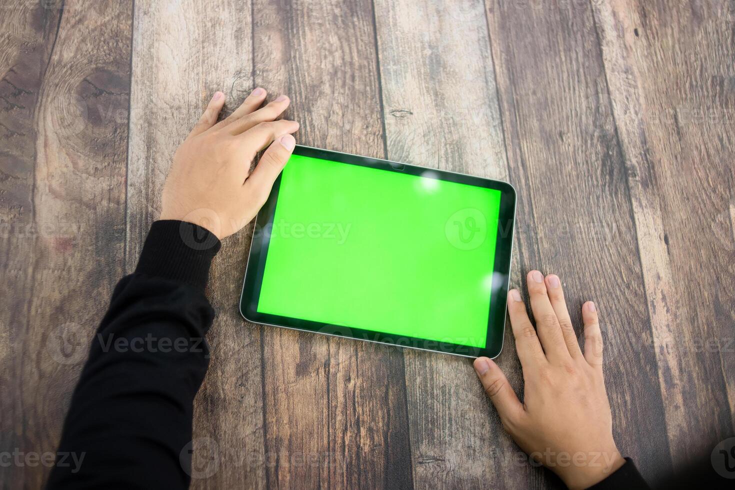 Mock up of a hand holding an iPad tablet with a greenscreen against a wooden texture background photo
