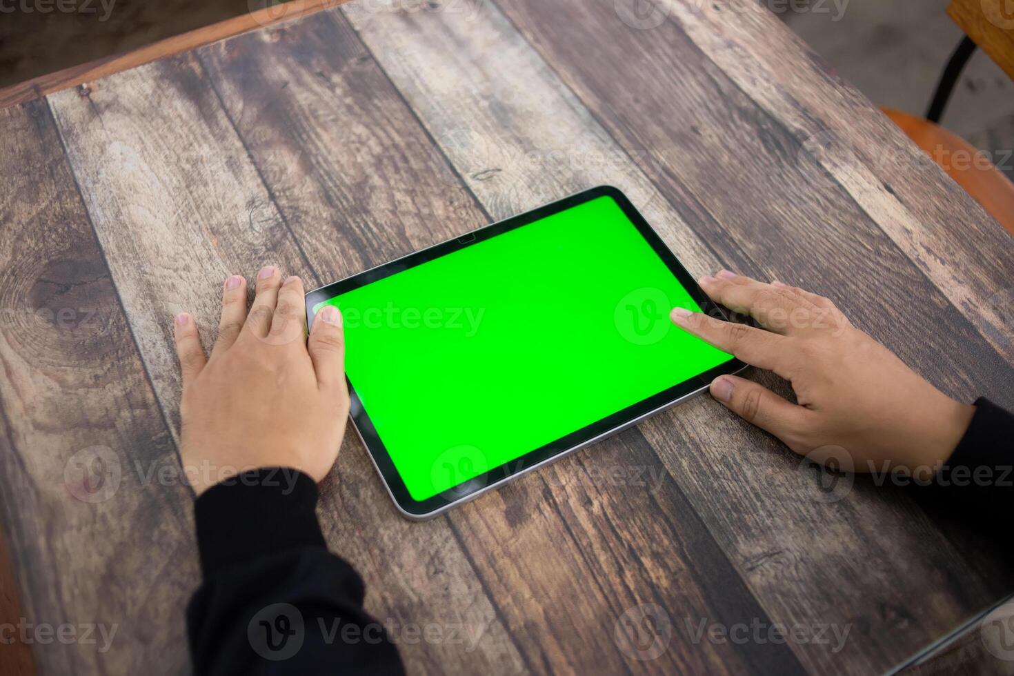 Mock up of a hand holding an iPad tablet with a greenscreen against a wooden texture background photo
