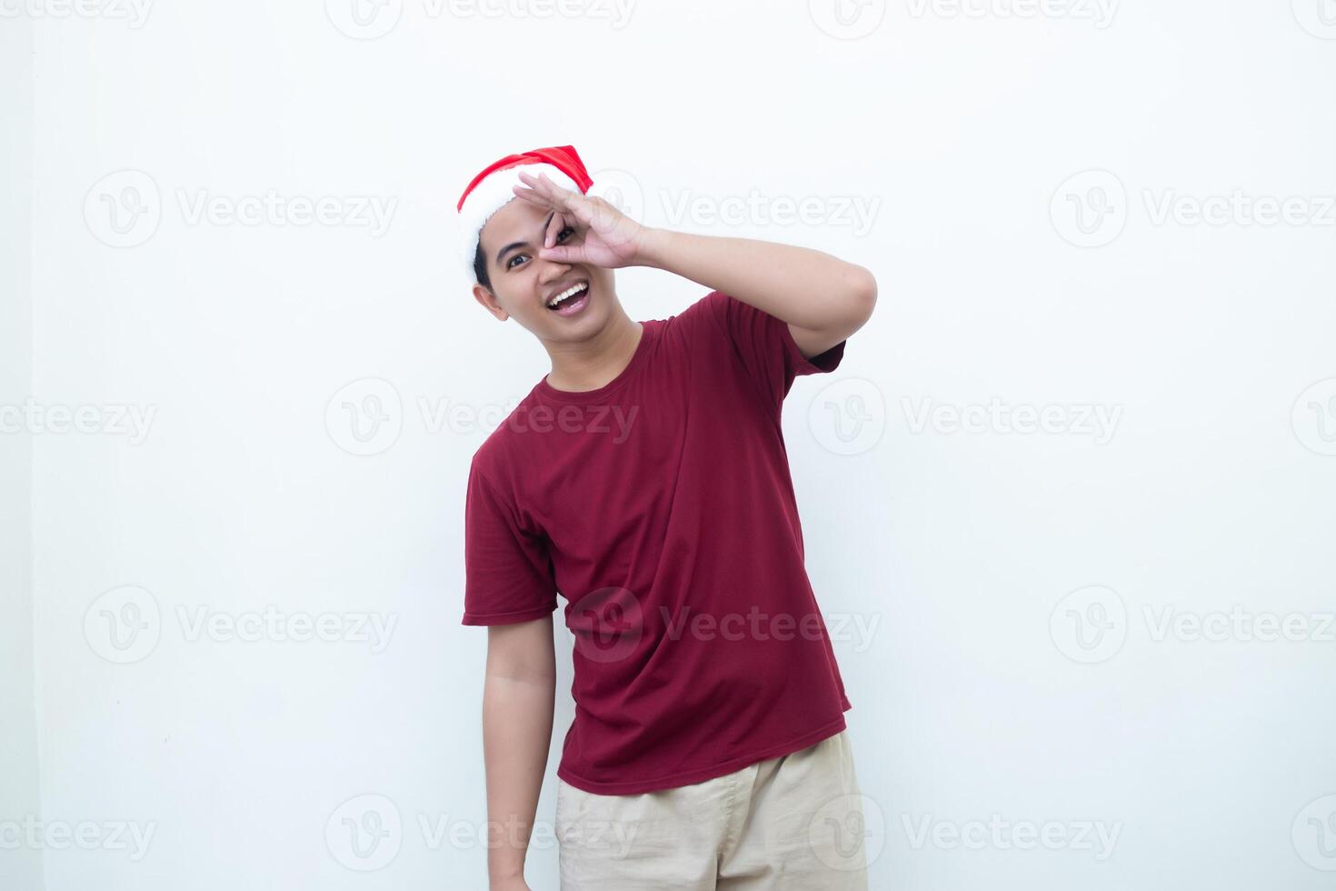 Young Asian man wearing a Santa Claus hat with a hand making the ok gesture isolated by a white background for visual communication photo