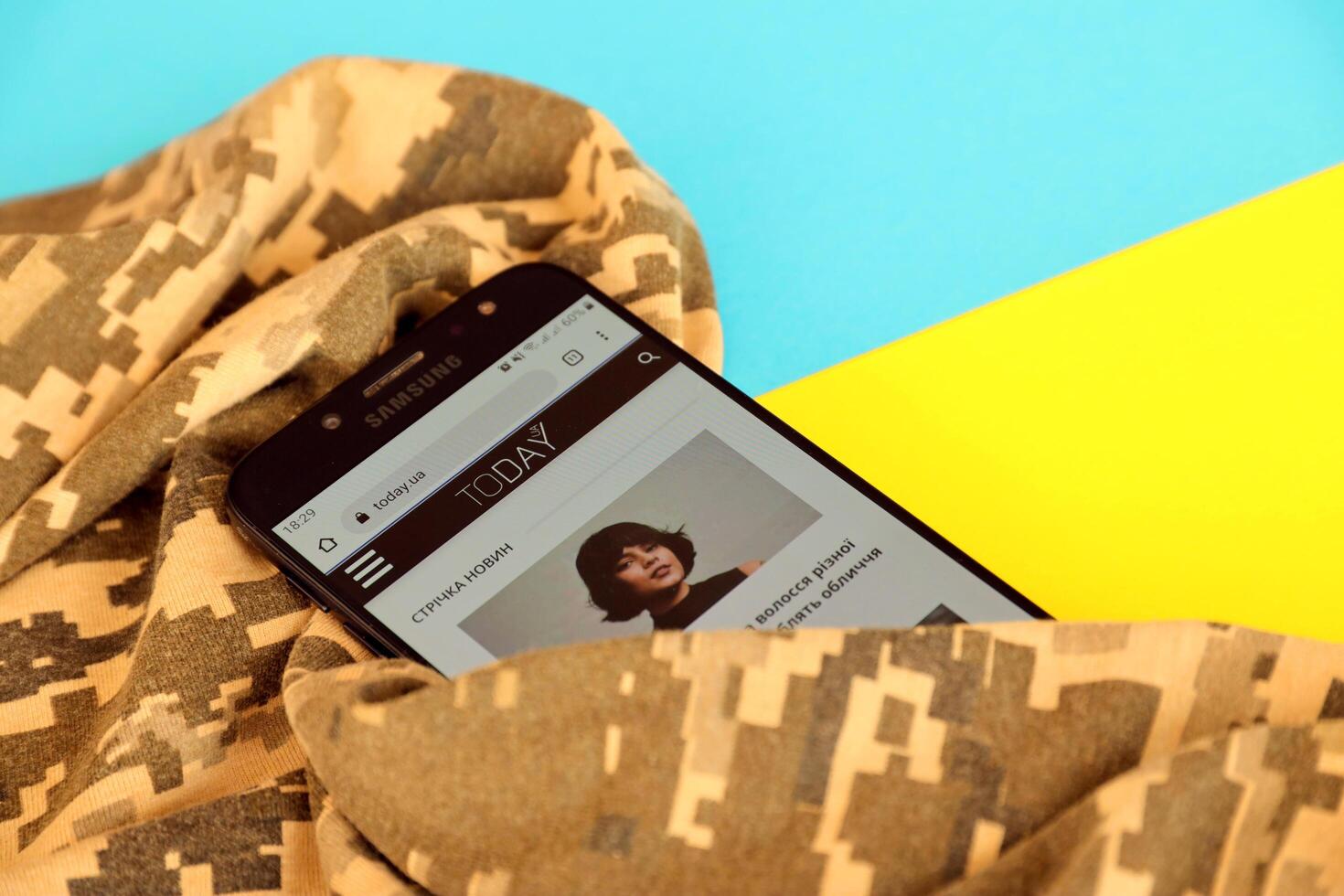 KYIV, UKRAINE - 4 MAY, 2023 Today UA ukrainian news portal on smartphone screen with ukrainian flag and camouflage fabric photo