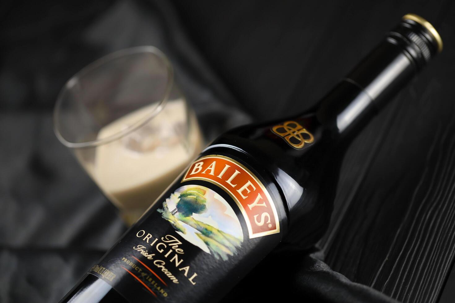 KYIV, UKRAINE - MAY 4, 2022 Baileys original alcohol bottle on wooden table with black fabric photo