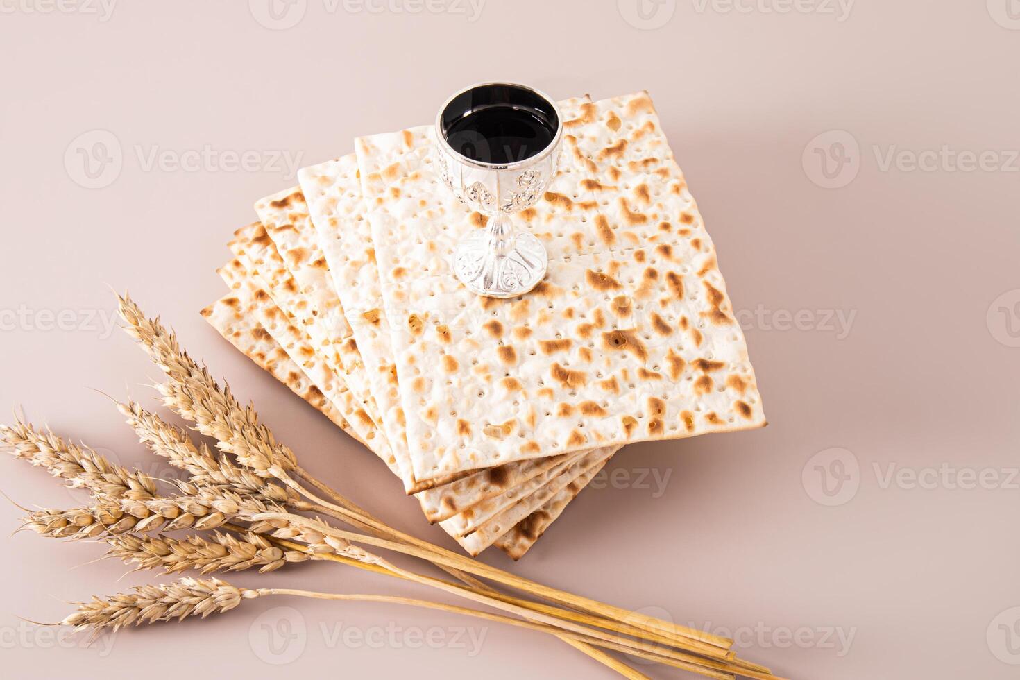 A silver glass of red wine stands on a stack of matzoth slices on a beige background with ears of corn. Concept of the Jewish Passover holiday. photo