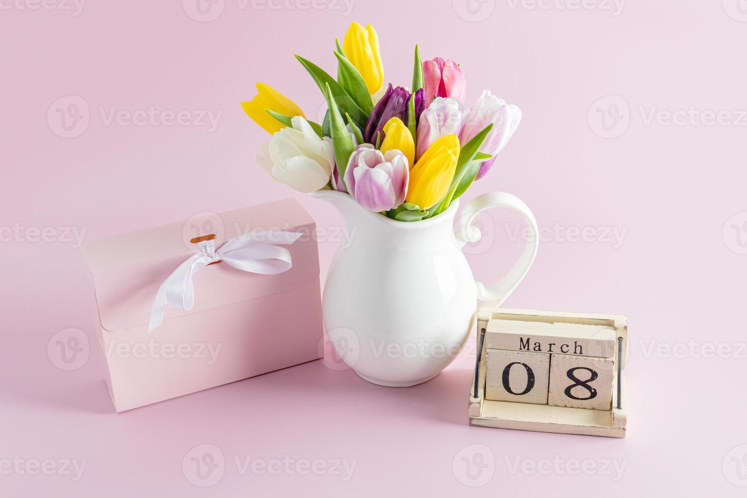 ramo de flores de primavera tulipanes en un blanco jarra en un rosado antecedentes siguiente a un fiesta caja y un de madera calendario con el fecha de el octavo de marzo día festivo. foto