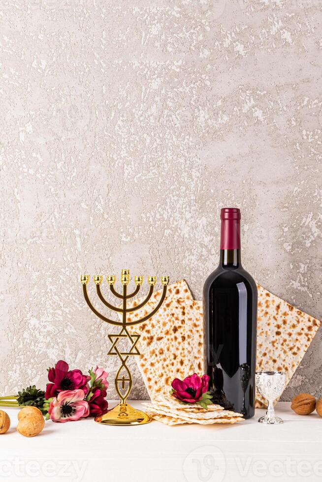 Vertical festive background for Jewish Passover holiday with traditional matzoth bread, red wine, flowers and golden minor candlestick. A copy space. photo