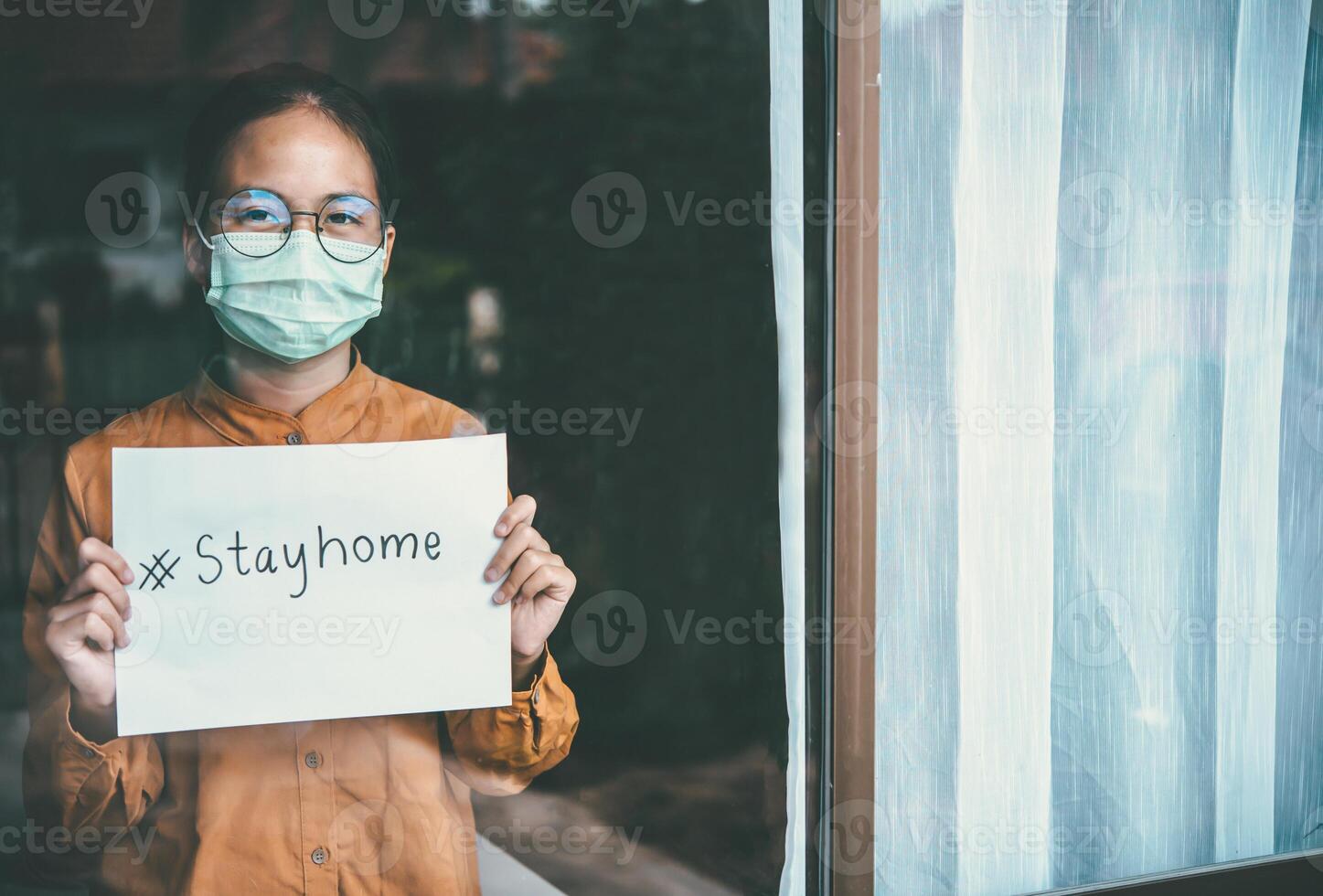 asiático niña vistiendo anteojos, vistiendo un mascarilla, participación papel etiquetado quedarse en casa, es aburrido de teniendo a detener y tratar el enfermedad a hogar solo. concepto hogar cuarentena, prevención covid-19 foto