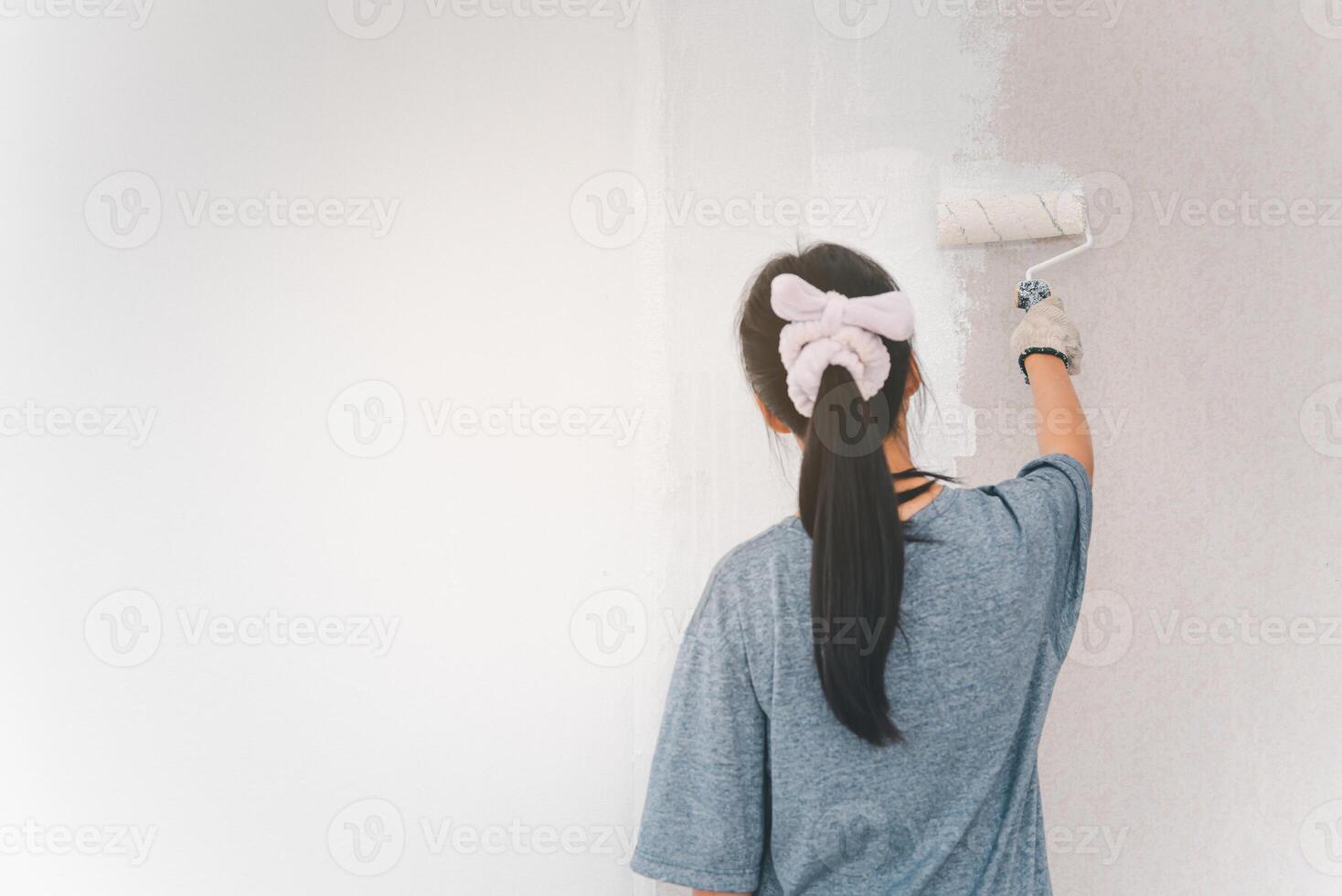 Young woman painting the walls with a roller using white paint. photo