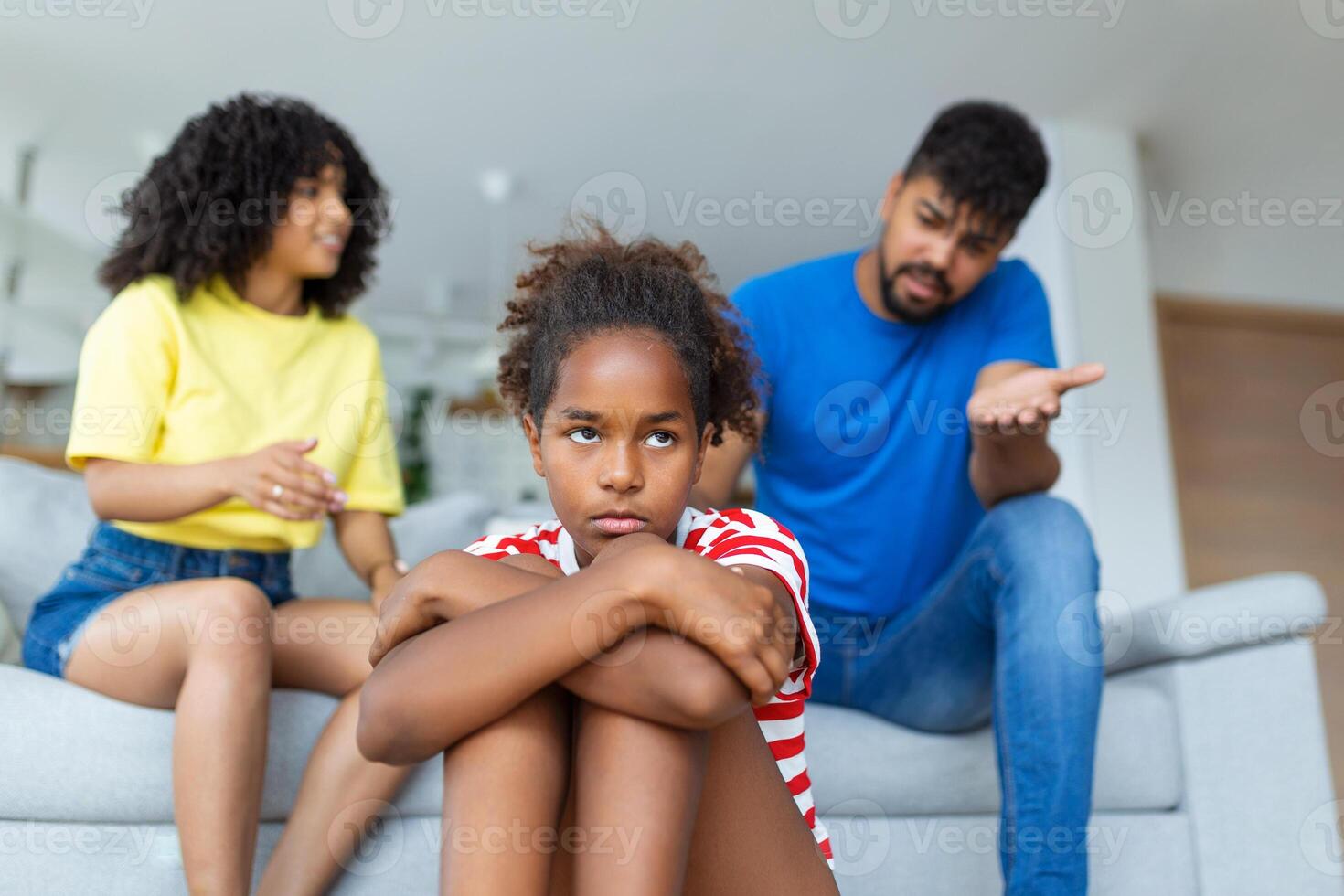 familia malentendido, infancia problemas. triste ofendido negro hija sentado en el piso, torneado espalda a padres después pelea a hogar, trastornado mamá y papá preguntando resentido niña qué incorrecto foto