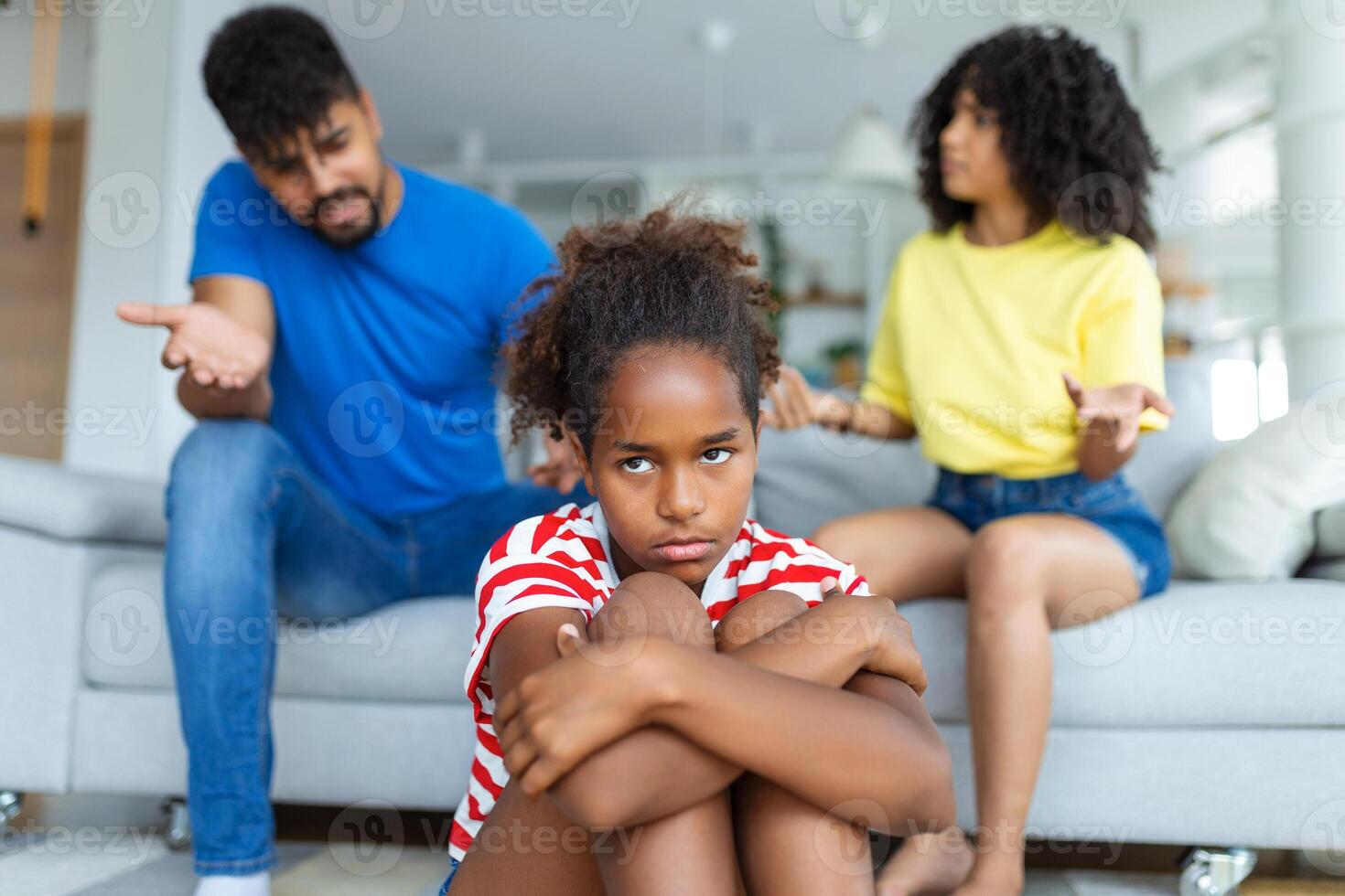 familia malentendido, infancia problemas. triste ofendido negro hija sentado en el piso, torneado espalda a padres después pelea a hogar, trastornado mamá y papá preguntando resentido niña qué incorrecto foto