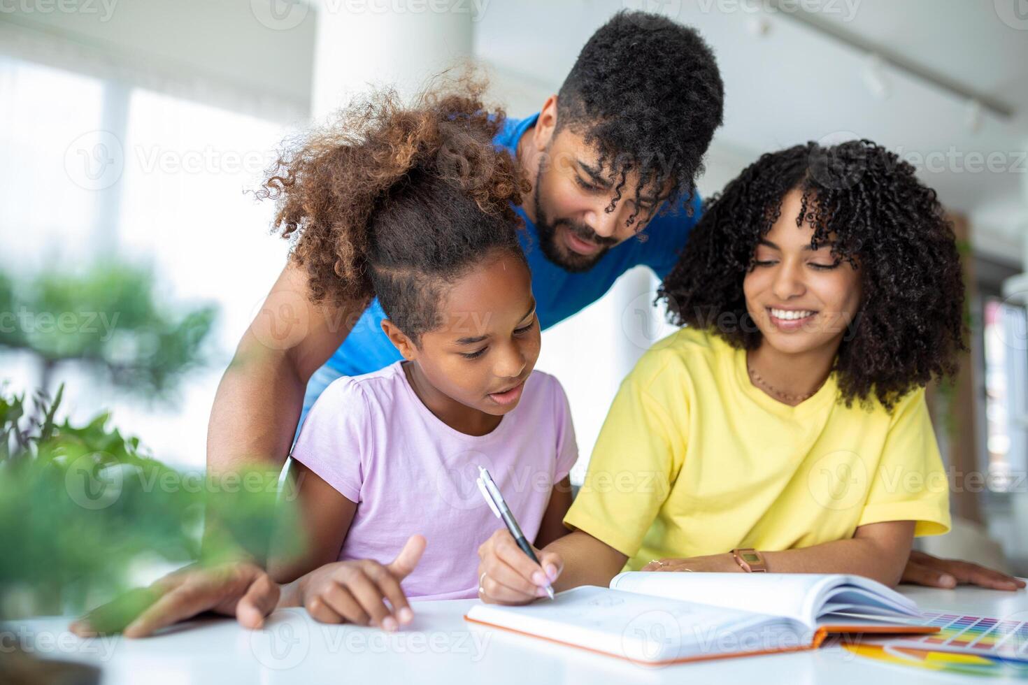 Multiethnic parents helping daughter with her homework at home. Young father and mother helping daughter study at living room. Little girl completing her exercises with the help of dad and mom. photo