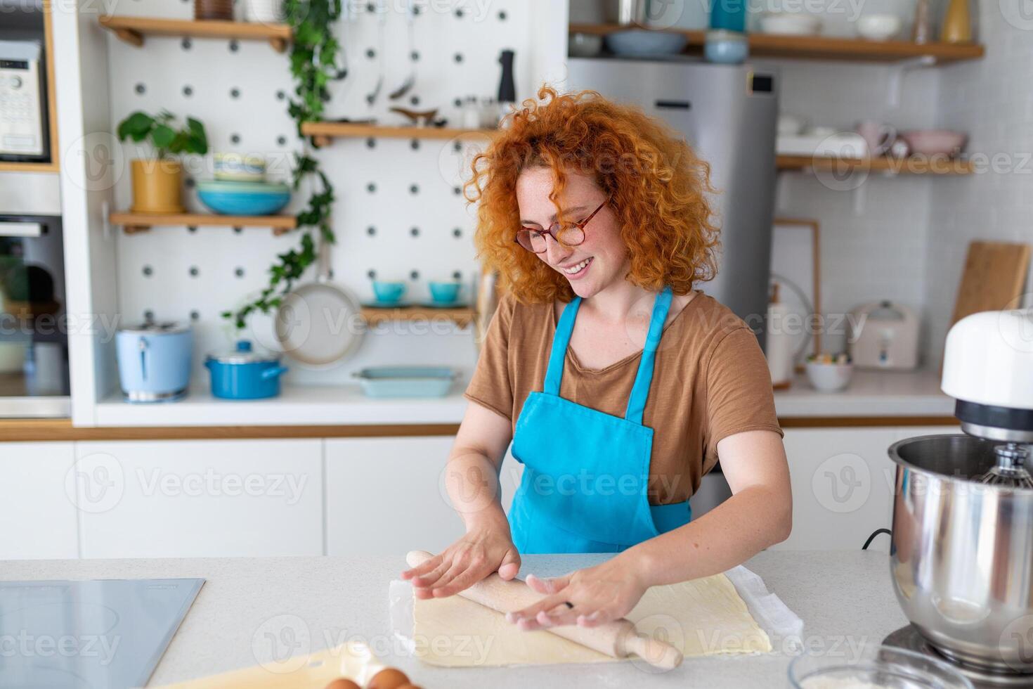 horneando concepto. retrato de alegre mujer amasadura masa en cocina interior, alegre hembra en delantal teniendo divertido mientras preparando hecho en casa Pastelería, foto