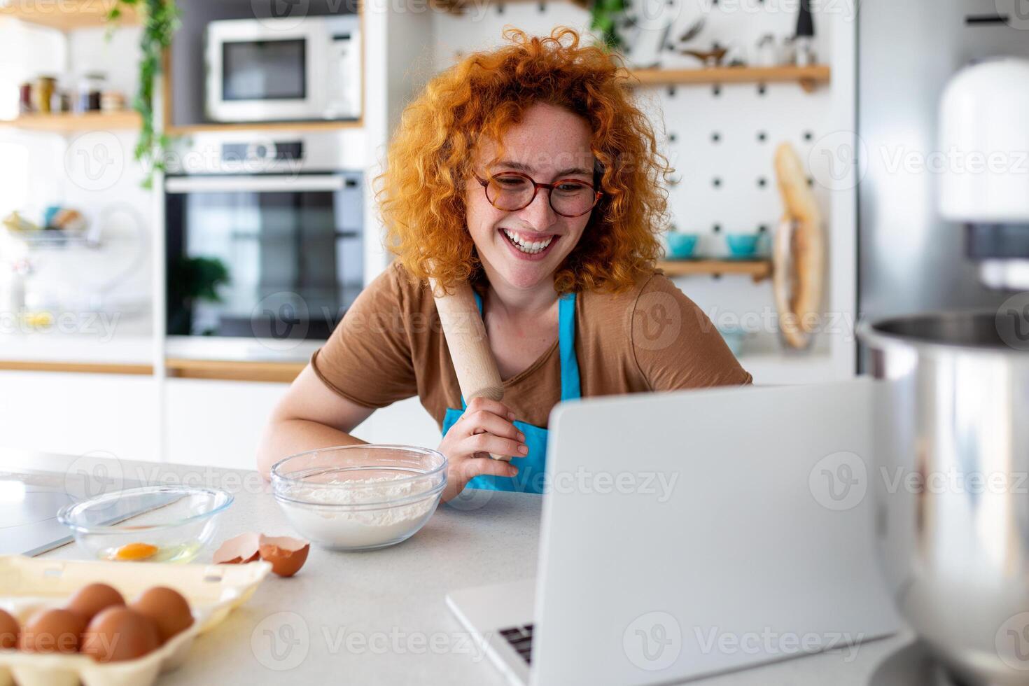 A young woman learns to cook, she watches video recipes on a laptop in the kitchen and cook a dish . Cooking at home concept photo