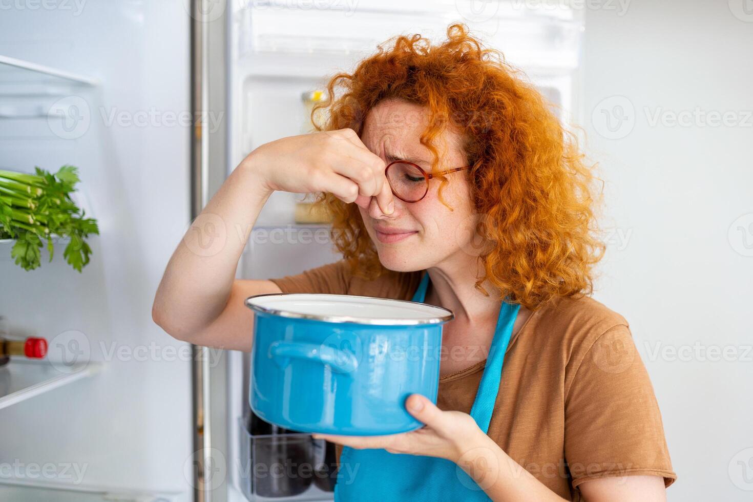 Bad Food In Fridge, young woman in holding her nose because of bad smell from food in refrigerator at home photo