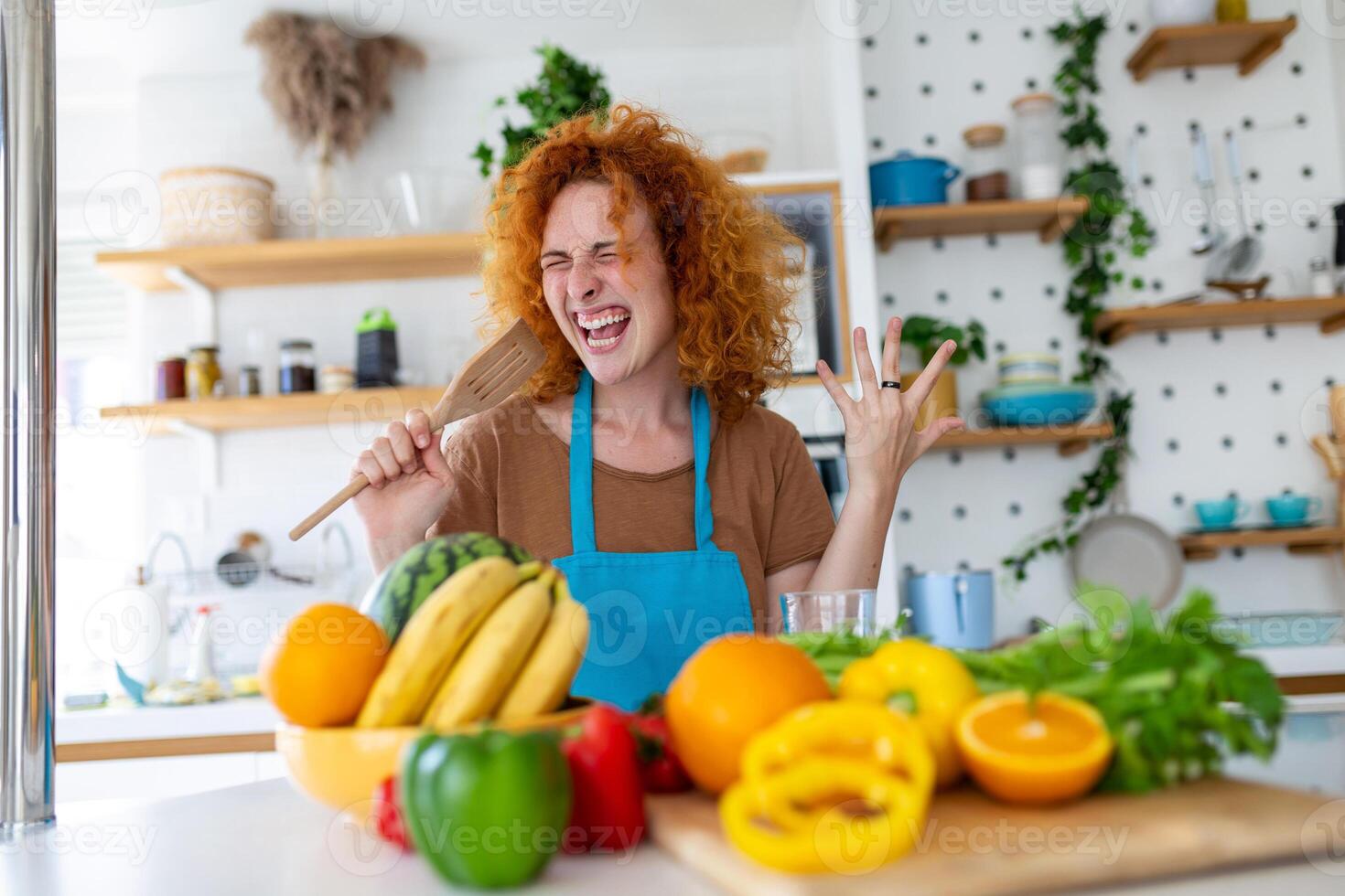 gracioso hermosa mujer canto dentro espátula, Cocinando en moderno cocina, participación espátula como micrófono, baile, escuchando a música, juguetón niña teniendo divertido con batería de cocina, preparando alimento. foto