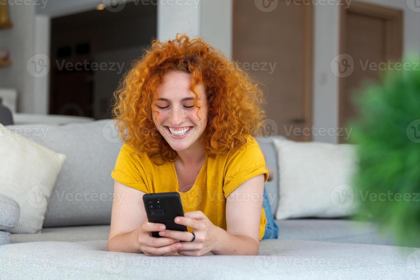 Woman using mobile phone while lying on sofa. Young female is resting at home. photo