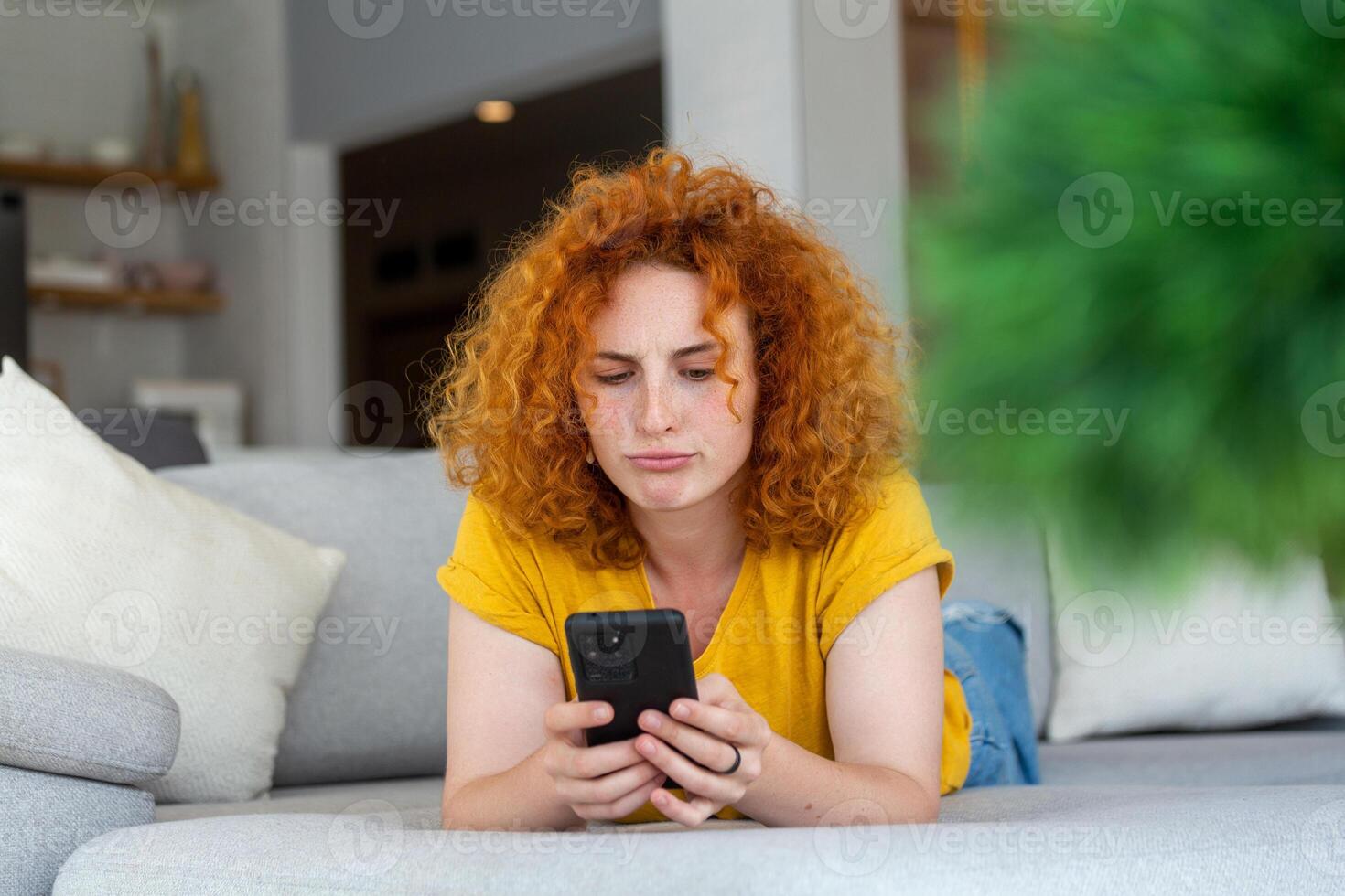 Woman using mobile phone while lying on sofa. Young female is resting at home. photo