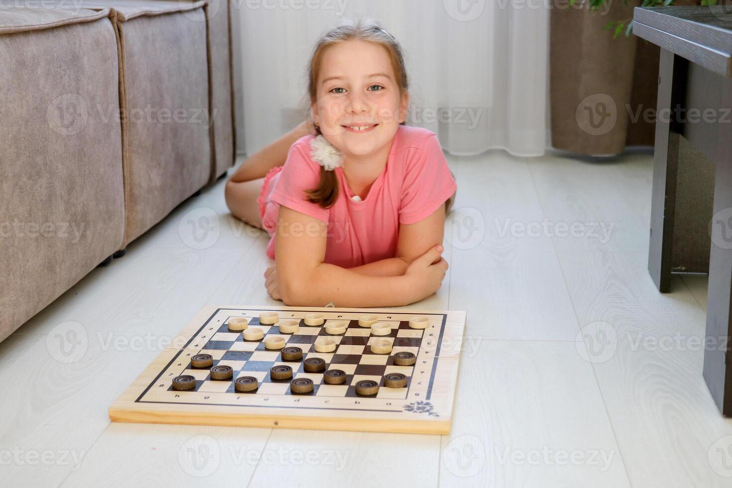 smiling girl lying on the floor at home next to checkers ready to play photo