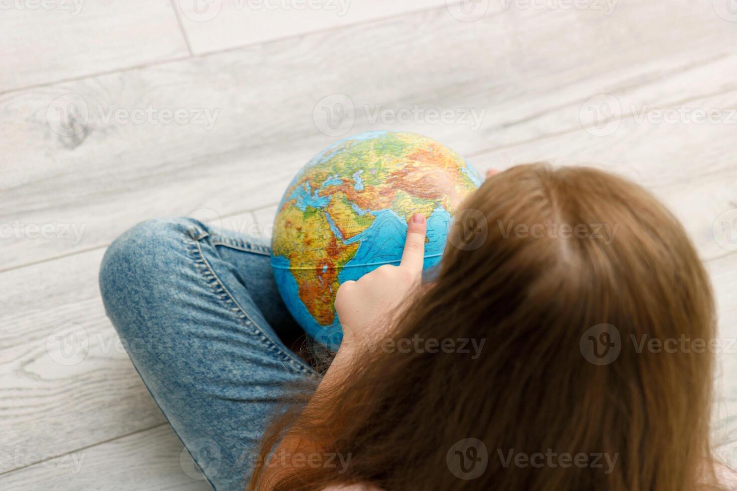 girl sitting on the floor unwinds the globe pointing her finger at India photo