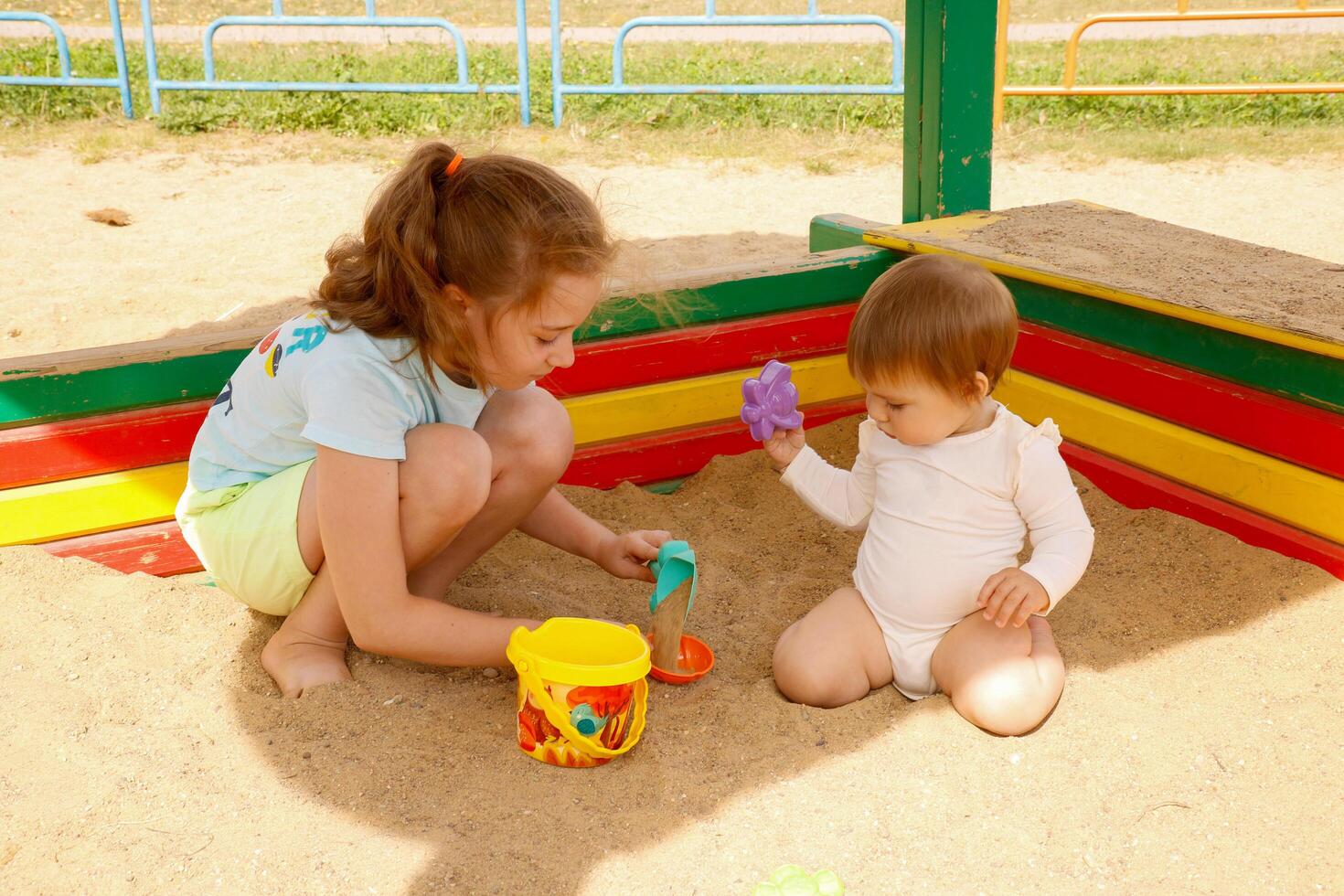 two sisters, older and younger, play in the sandbox photo