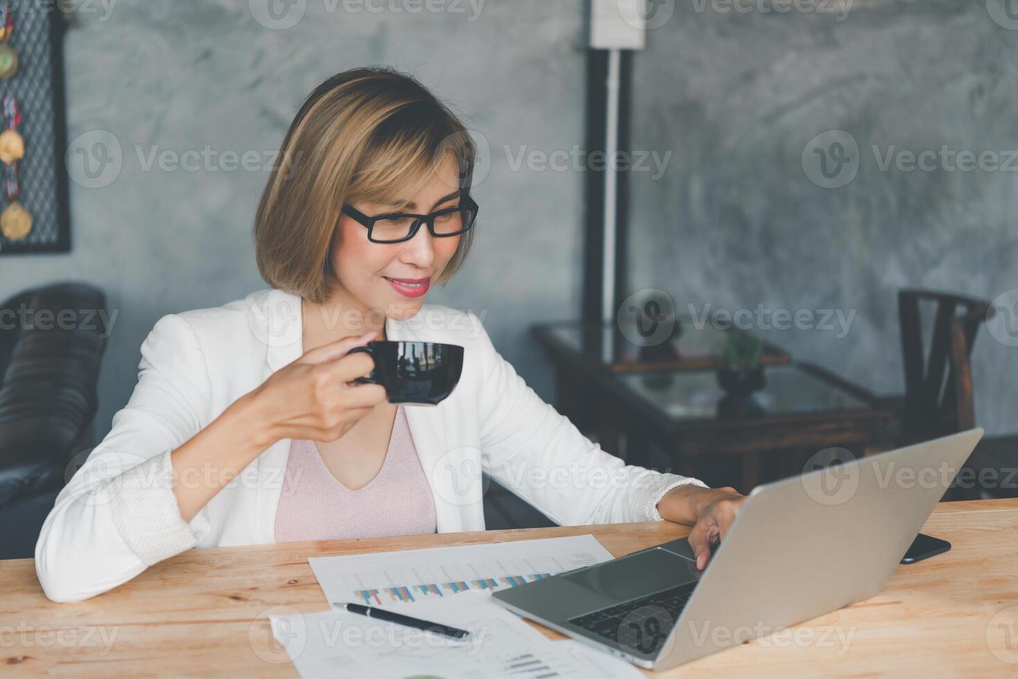 Business woman drinking coffee and working on laptop searching web, browsing information sitting doing work at desk photo