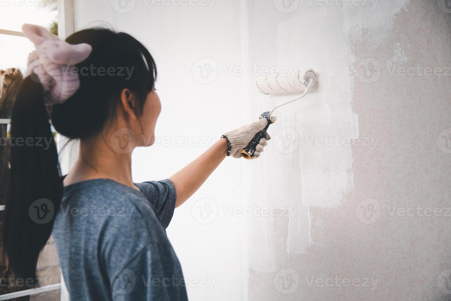 Young woman painting the walls with a roller using white paint. photo