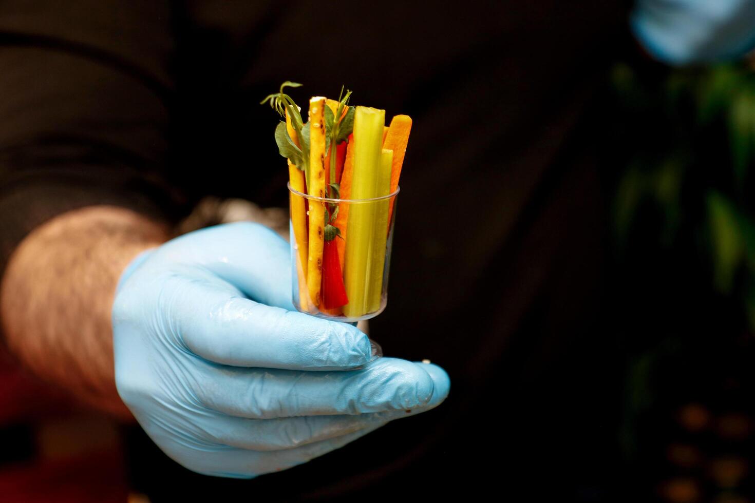 a chef's hand in a glove holds out portioned vegetables photo