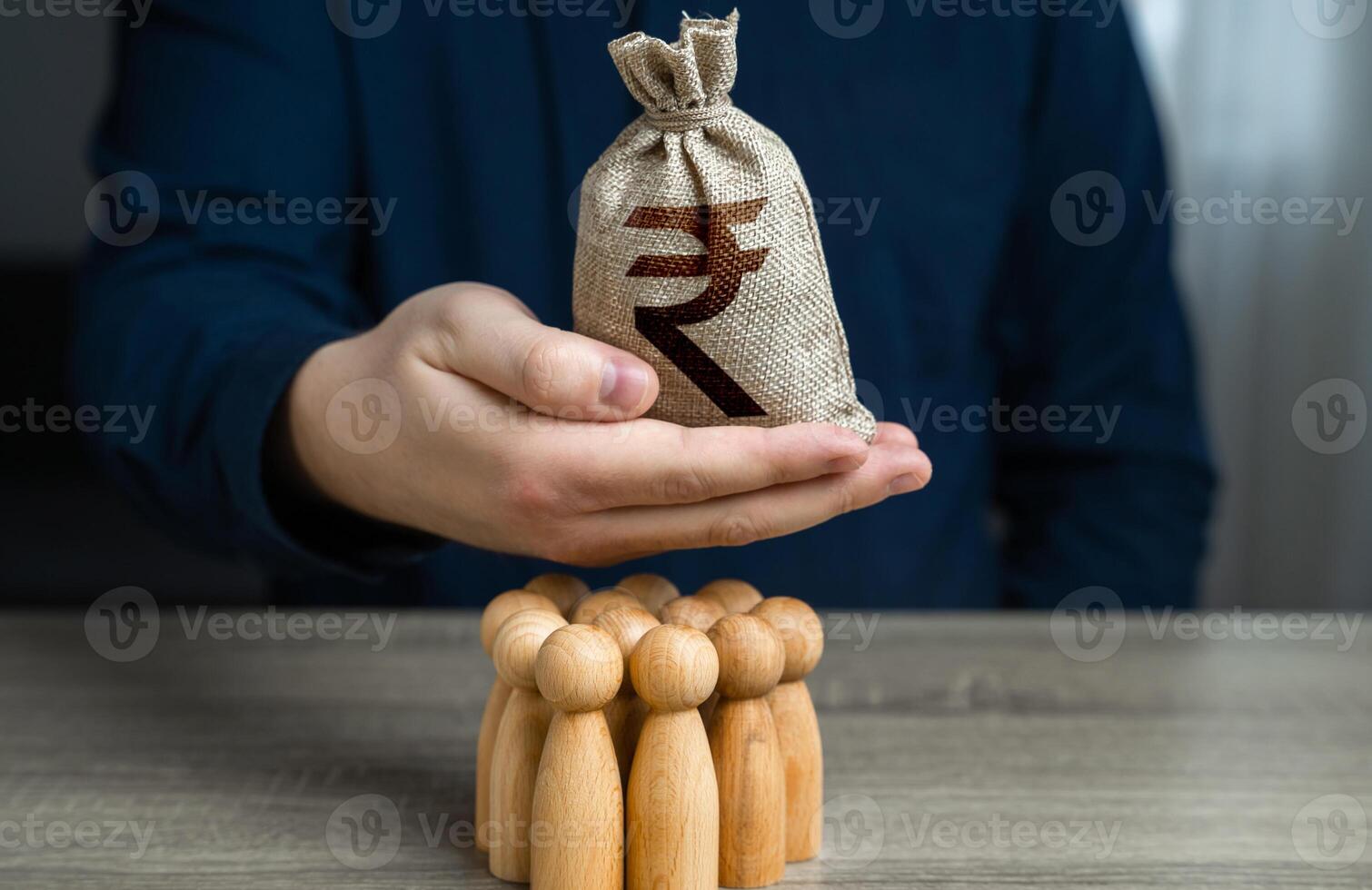 A man is holding a indian rupee money bag over a group of people figurines. Political lobbying. Organization of the community budget. Payment for labor. Generation of funds from cooperation. photo