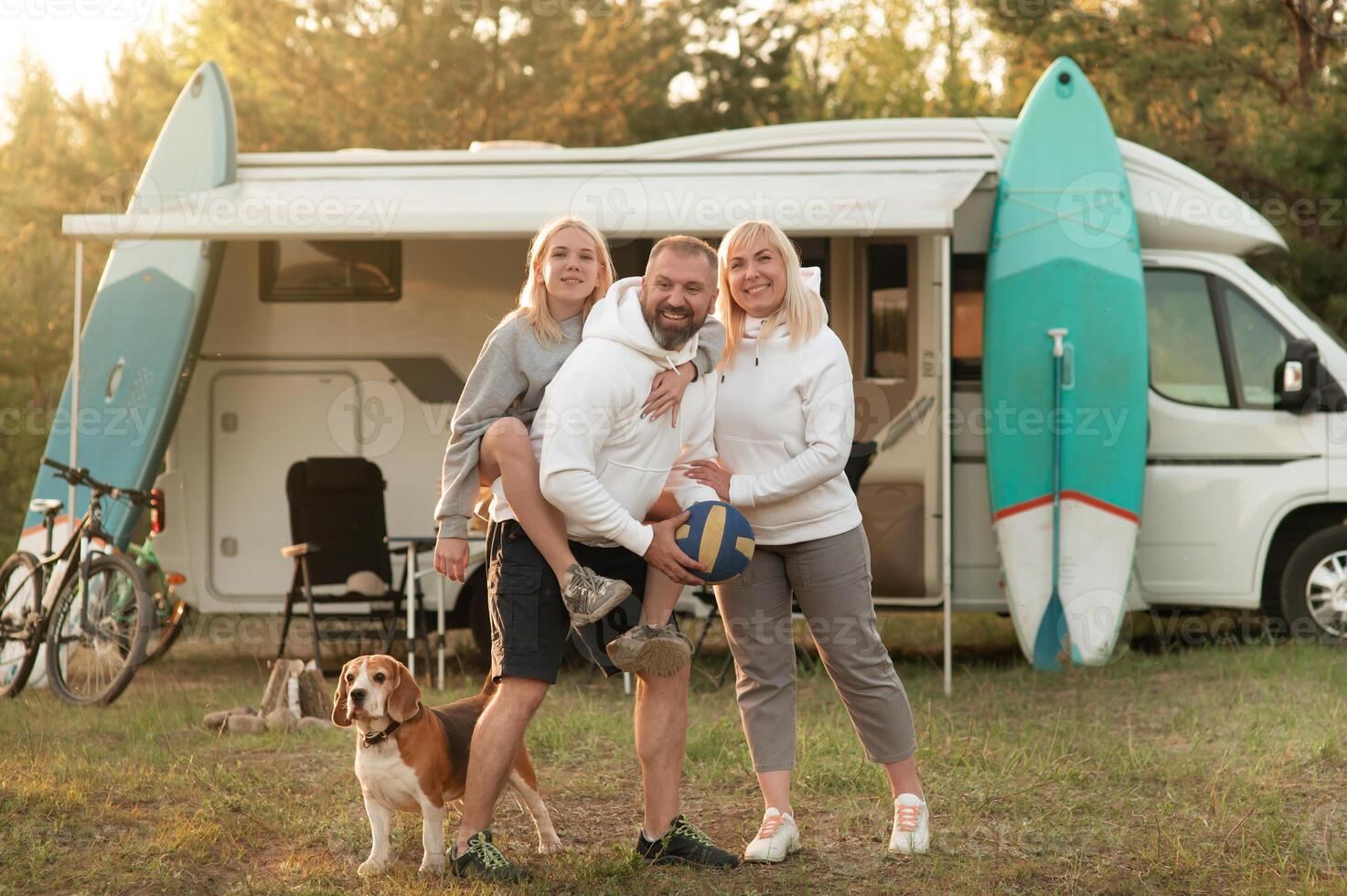 Happy parents with their child playing with a ball near their mobile home in the woods photo