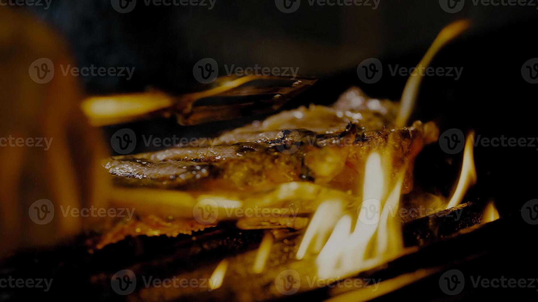 Grilled meat steak on stainless grill depot with flames on dark background. Food and cuisine concept. photo