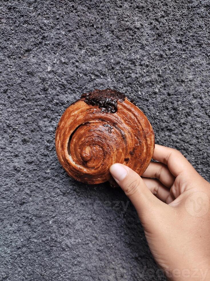 mano participación cromboloni, redondo cuerno, nuevo York rollo, un viral Pastelería combinatorio croissants y bomboloni en hormigón pared antecedentes. foto