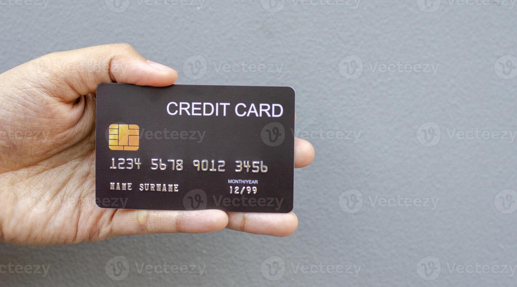 female hand holding a black credit card mockup with security chip embedded on a gray background with copy space photo