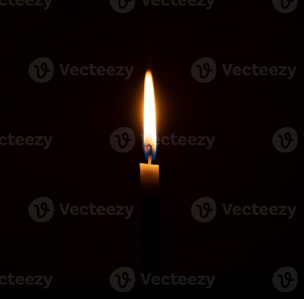 A single burning candle flame or light glowing on an orange candle on black or dark background on table in church for Christmas, funeral or memorial service with copy spac photo