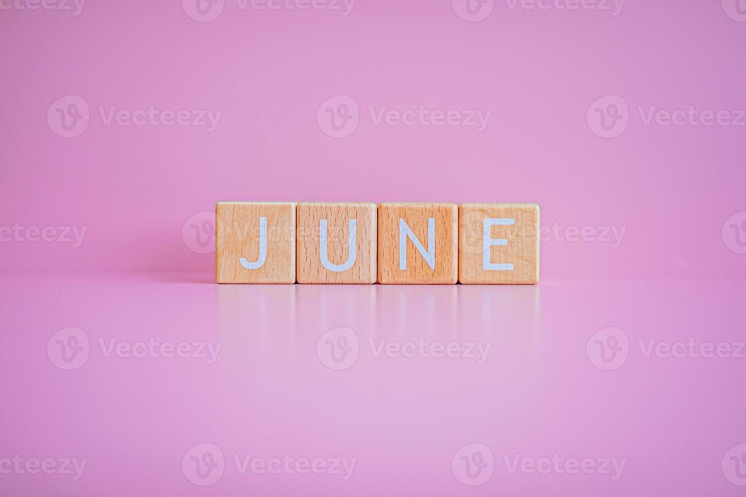 Wooden blocks form the text JUNE against a pink background. photo