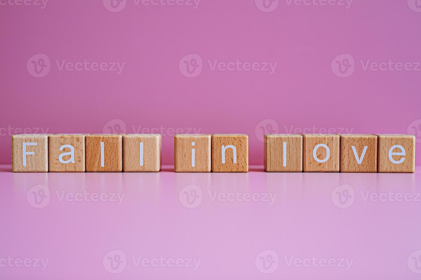 Wooden blocks form the text Fall in love against a pink background. photo