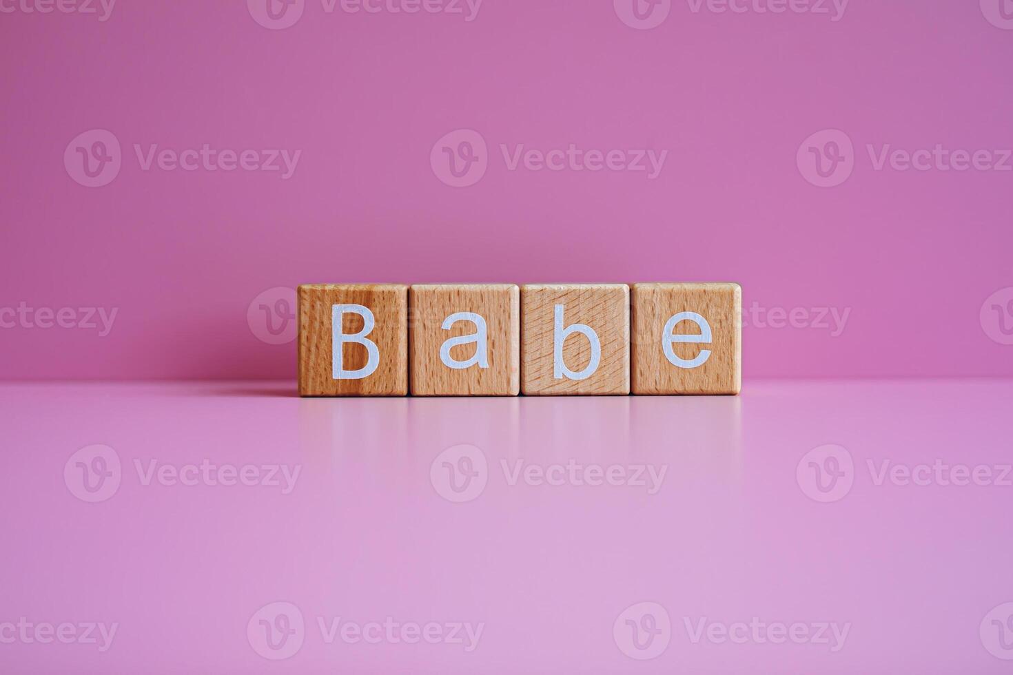 Wooden blocks form the text Babe against a pink background. photo