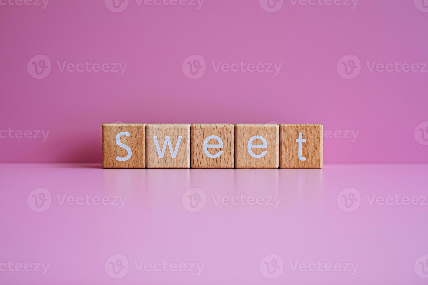 Wooden blocks form the text Sweet against a pink background. photo