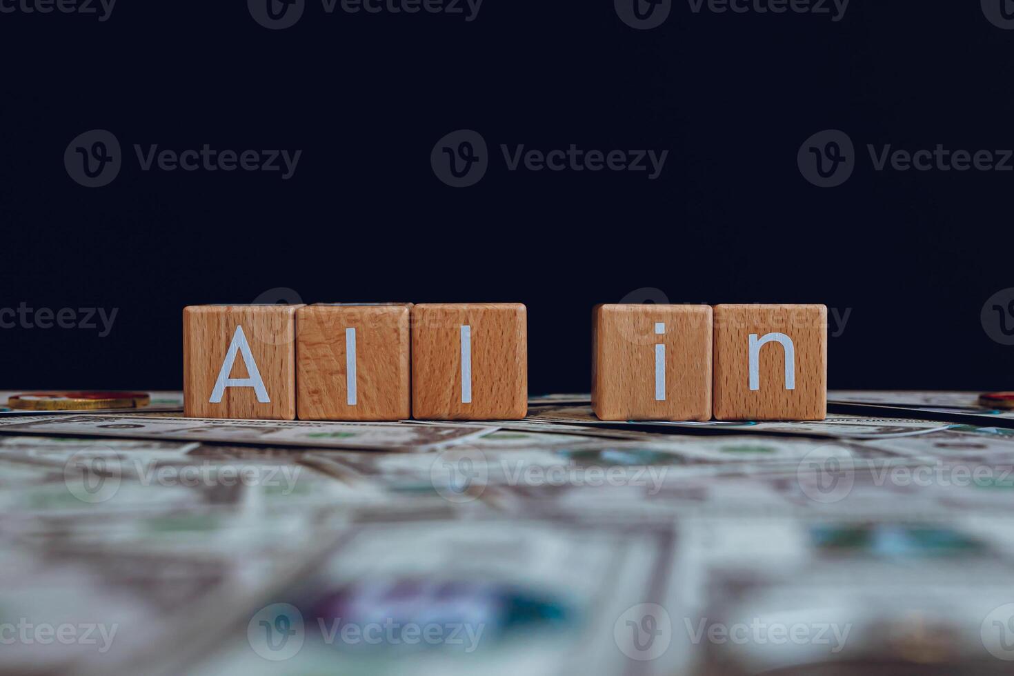 Wooden blocks with the text All in on a black background and crypto banknotes scattered on the ground. photo