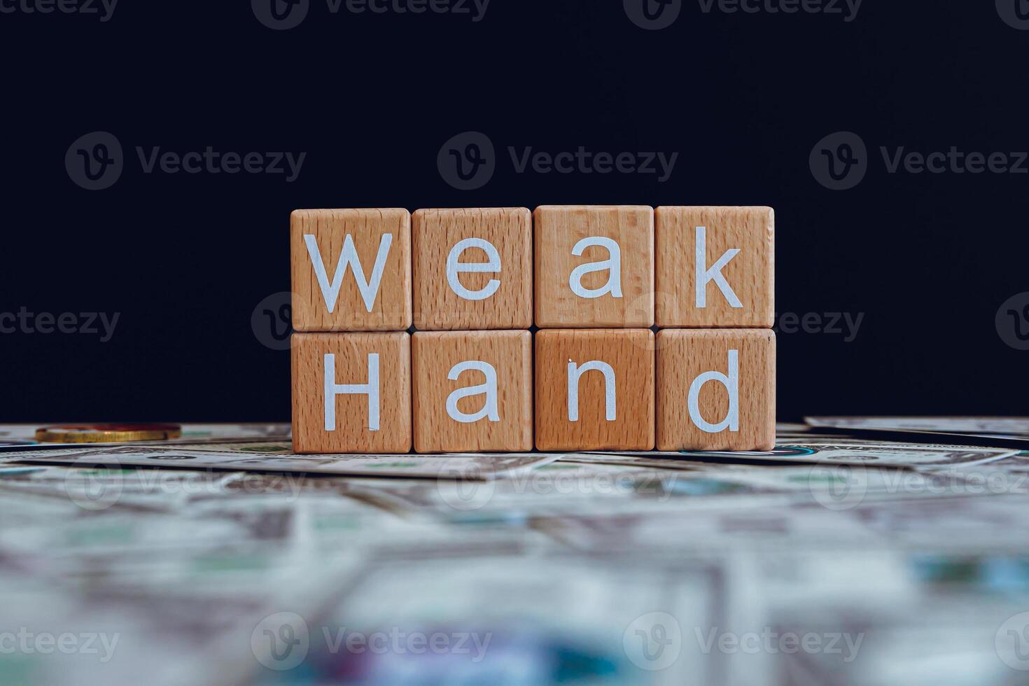 Wooden blocks with the text Weak Hand on a black background and crypto banknotes scattered on the ground. photo